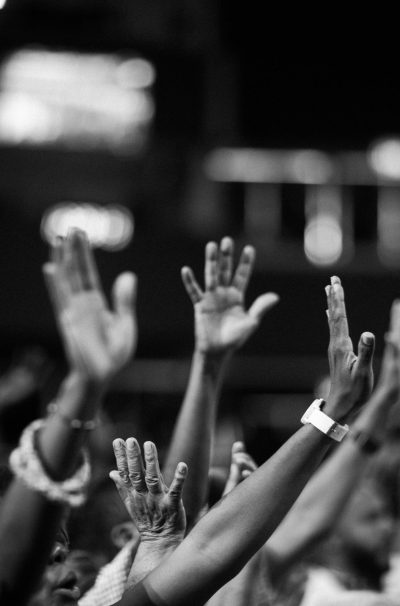 A group of people raising hands in a black and white concert setting, showing unity and celebration.